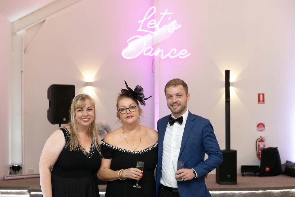 Guests dressed up for race day beside the Let's Dance neon at White Barn