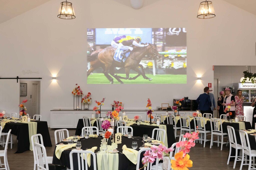 Melbourne Cup races projected on the mega screen above decorated luncheon tables
