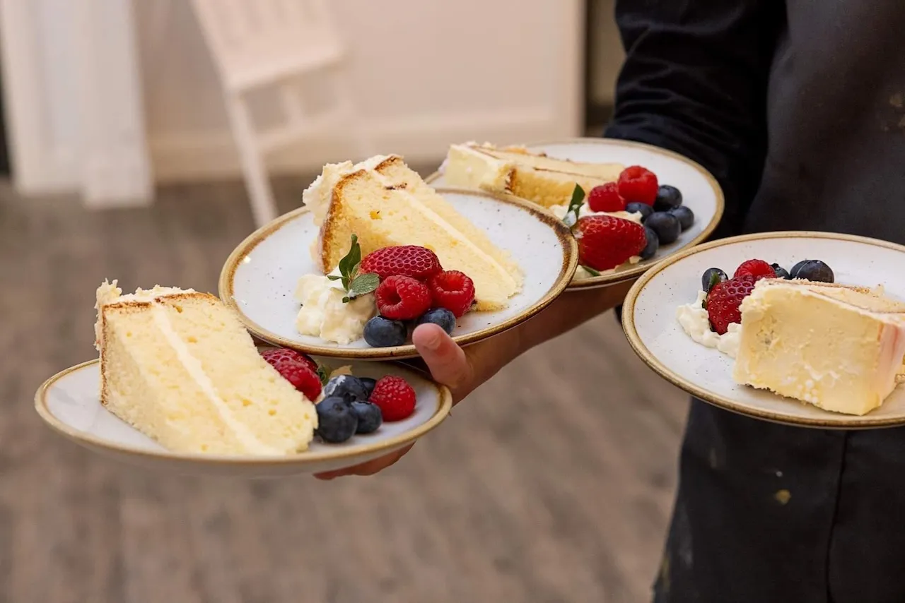 Close-up photo of wedding cake on plates served with berries and cream