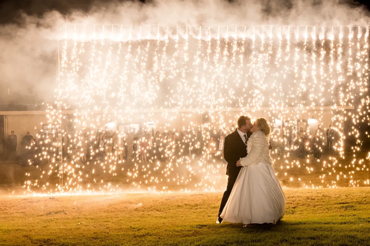 Photo of a Bride and Groom standing in front of a wall of sparkling ambers falling to the ground