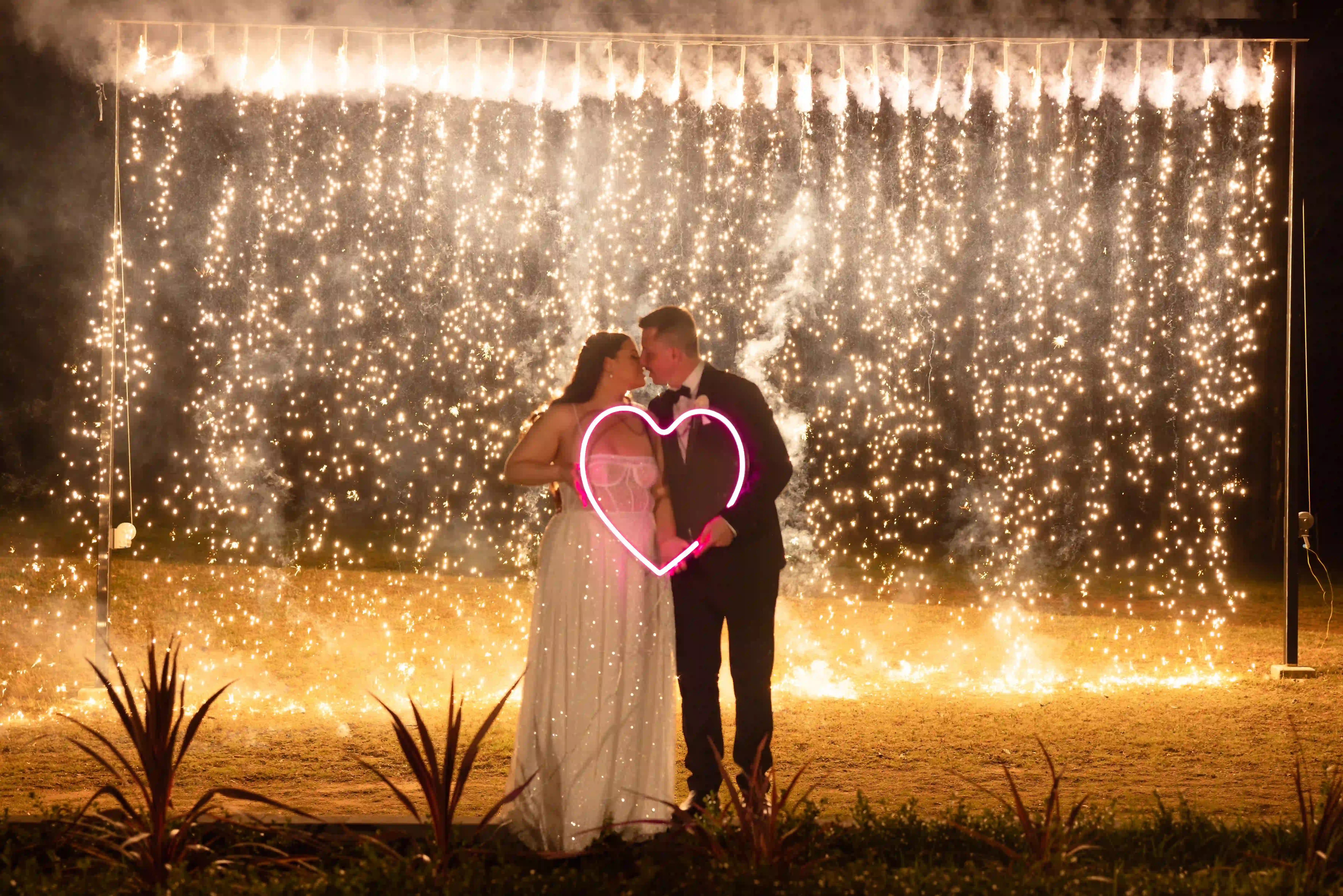 Photo of a Bride and Groom standing in front of a wall of sparkling ambers falling to the ground